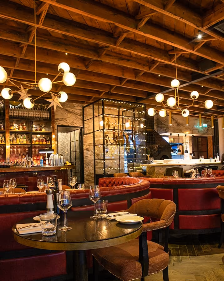 Cozy restaurant interior with wooden ceiling, red leather benches, round tables set with glassware.
