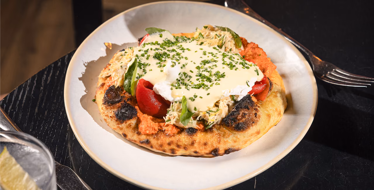 Small pizza with roasted red peppers, cheese, and basil leaves on a white plate on marble table.