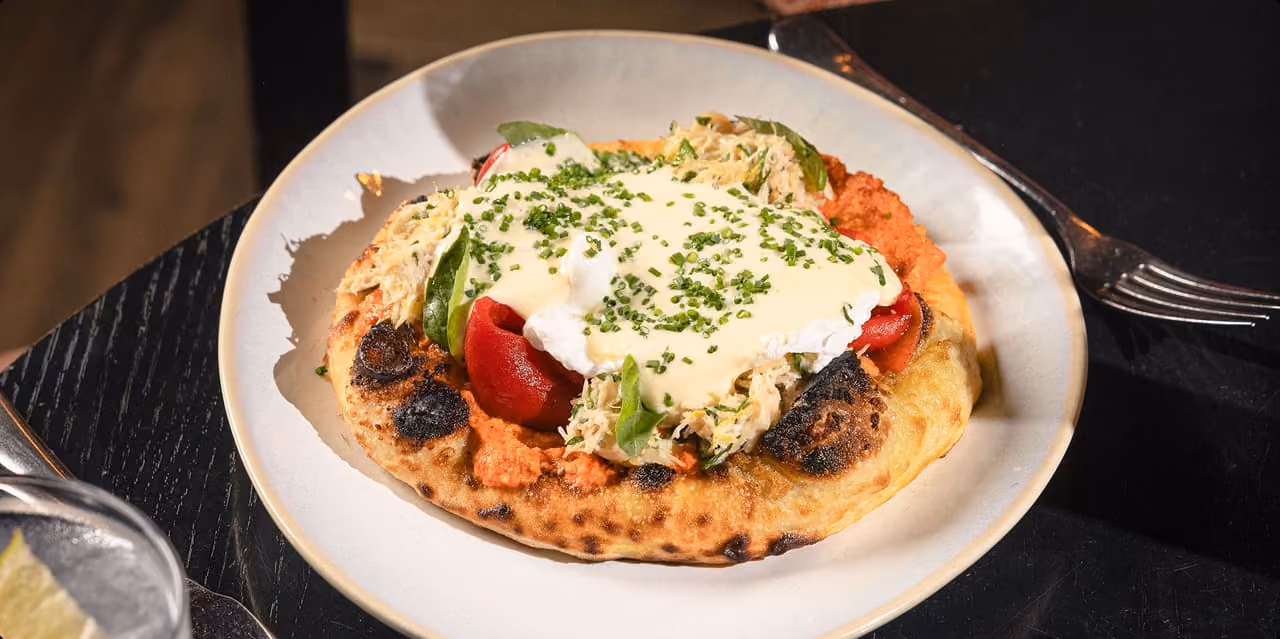 Small pizza with roasted red peppers, cheese, and basil leaves on a white plate on marble table.