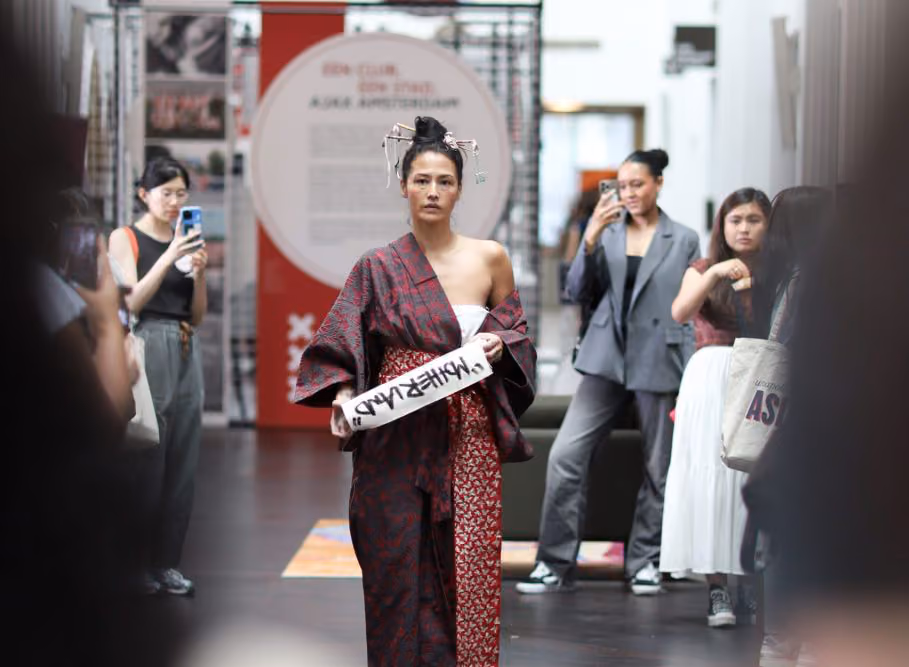 Performer in traditionele kleding met een bord in de hand tussen publiek in een tentoonstellingsruimte
