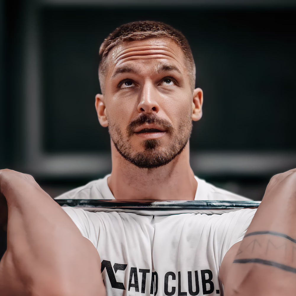 Mann mit Bart hebt Langhantel im Fitnessstudio und schaut nach oben.