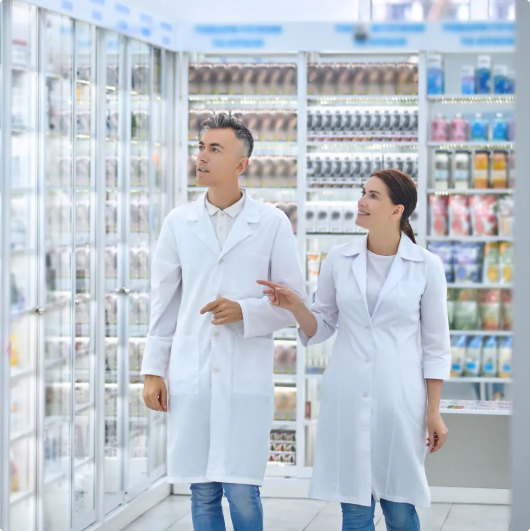 Two workers by refrigerated shop shelves