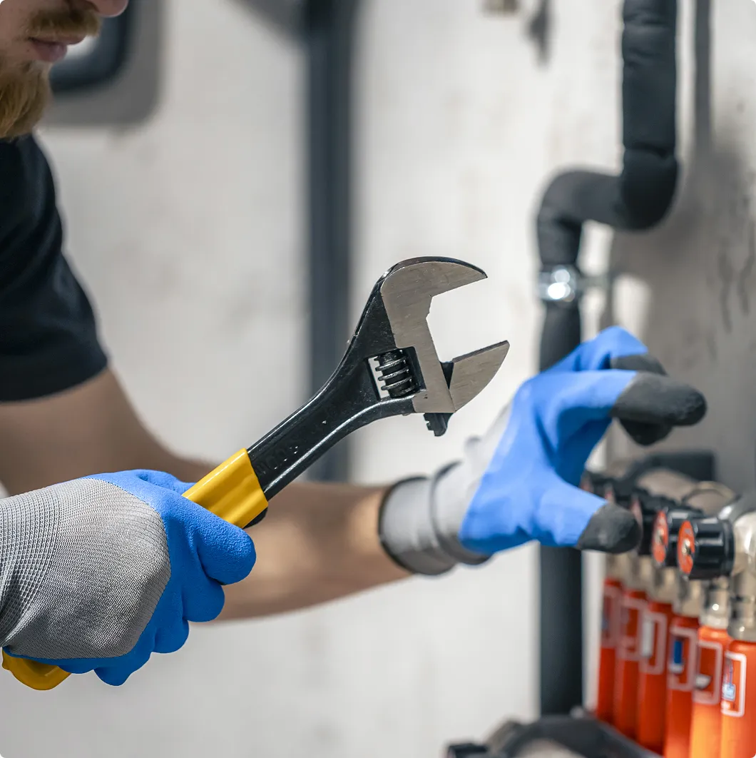 Gloved hands using a wrench on a boiler
