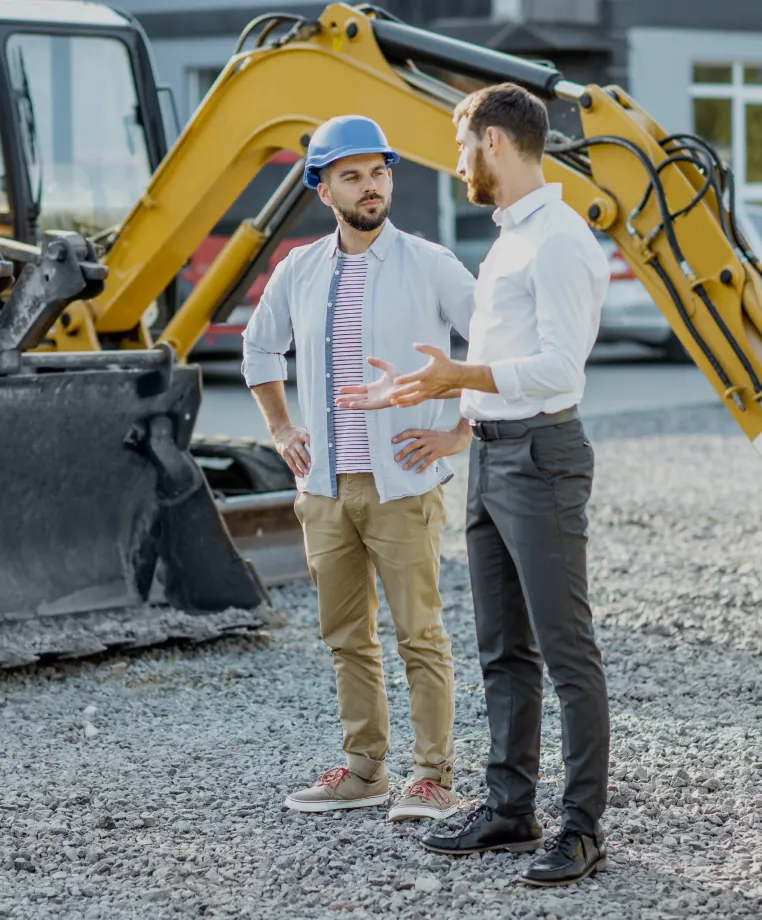 Two men talking in front of an excavator
