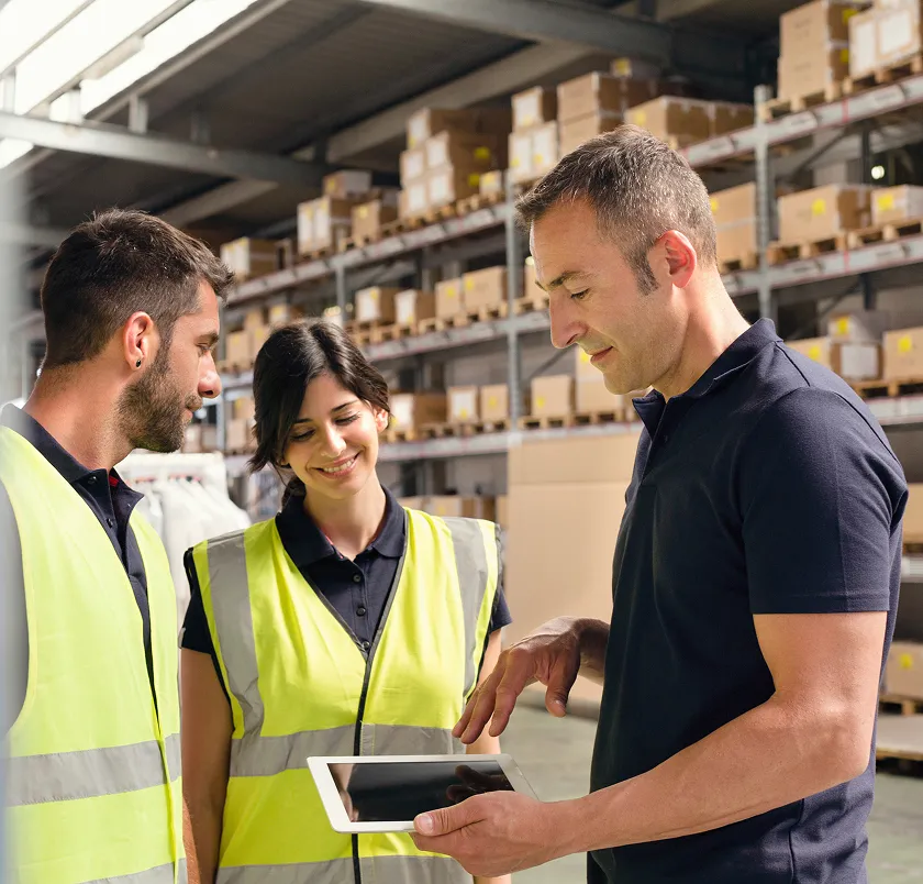 Three workers in hi-vis discussing work with a tablet in a warehouse