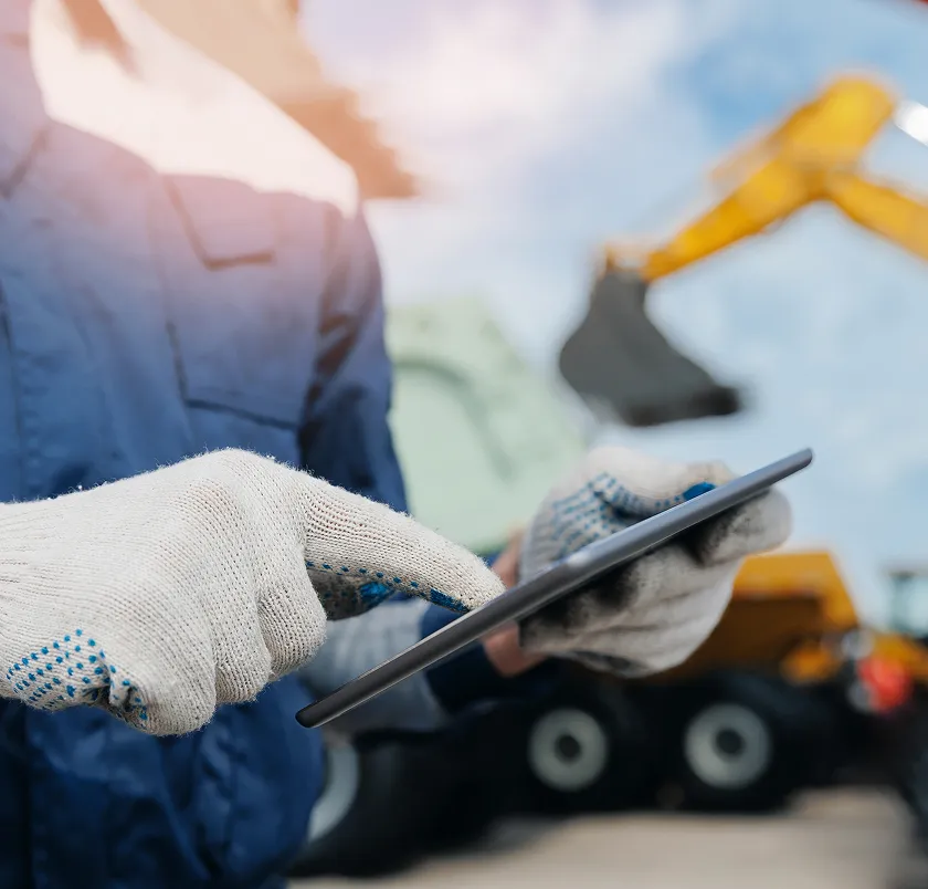 Gloved hand holding a tablet in front of an excavator