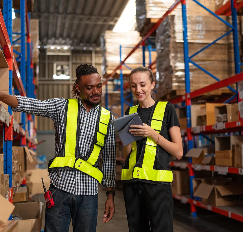 Two warehouse workers in hi-vis using a tablet by racking