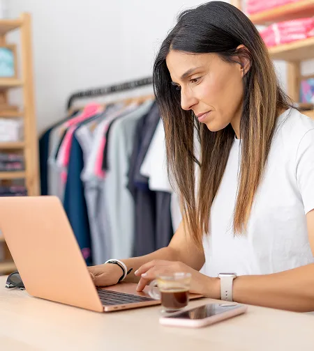 Woman using a laptop by clothing rails