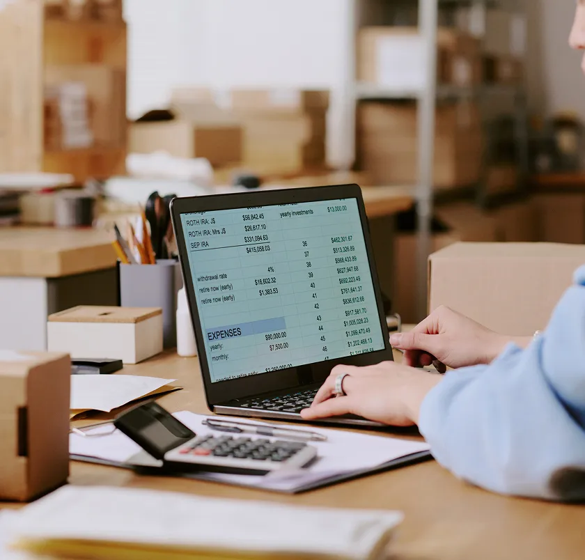 Person using a laptop and calculator beside parcels