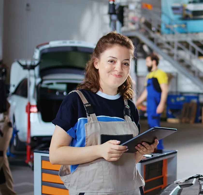 Smiling worker holding a tablet beside a van in a workshop