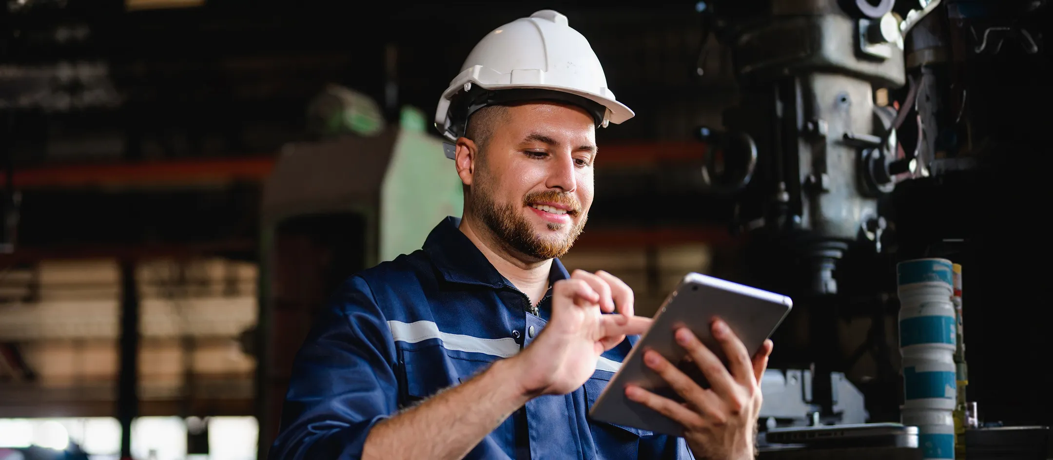 Worker in a hard hat using a tablet beside machinery