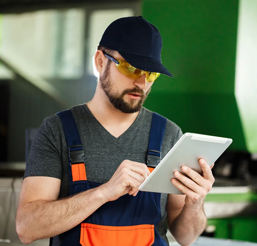 Worker in a cap and safety glasses using a tablet