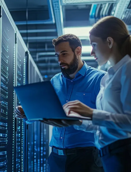 Two IT staff using a laptop in a server room