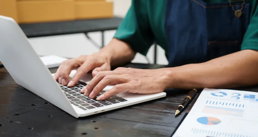 Hands typing on a laptop beside printed charts