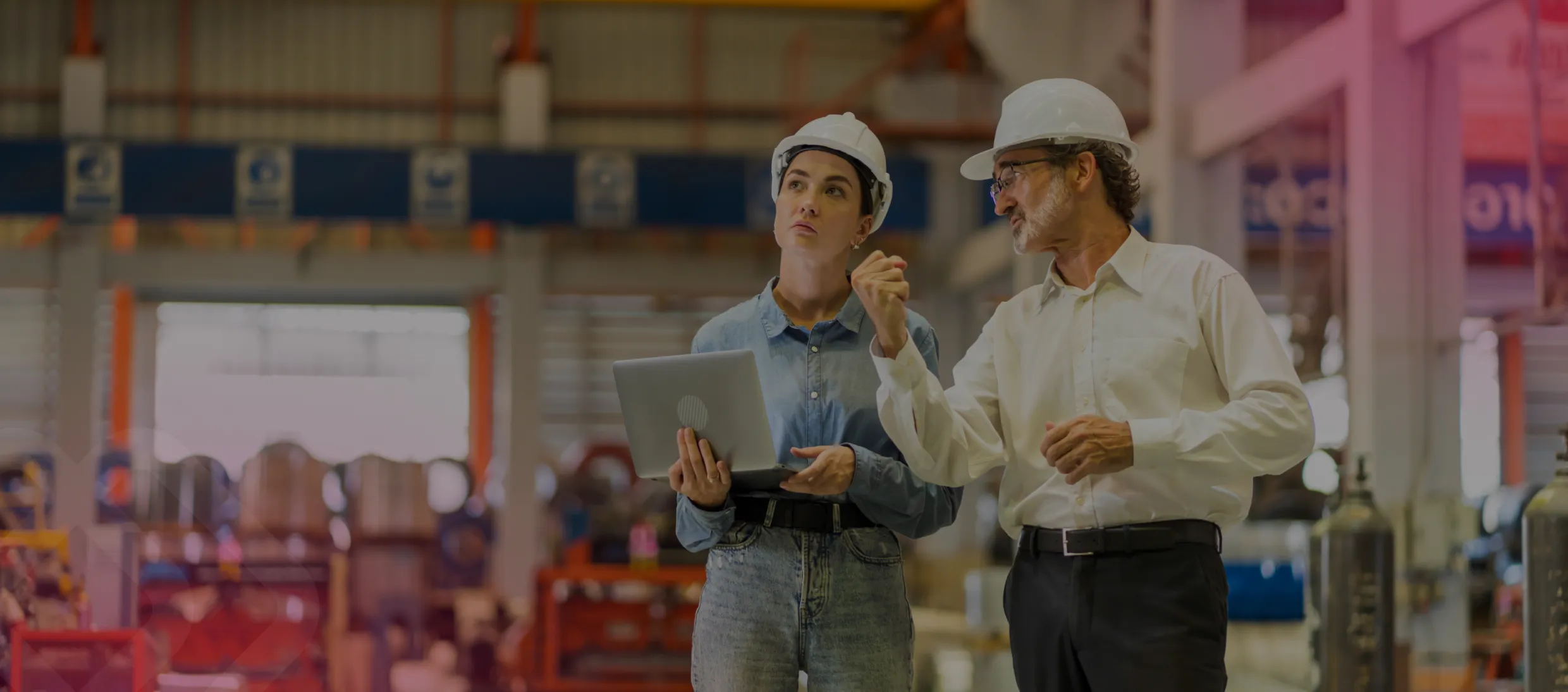 Two workers in hard hats talking in a warehouse