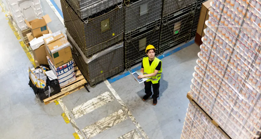 Worker in hi-vis with a laptop by pallets
