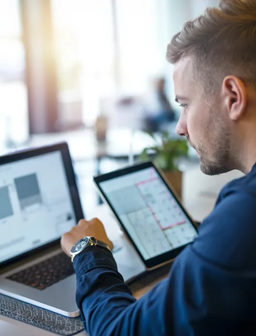 Man using a laptop and tablet at a desk