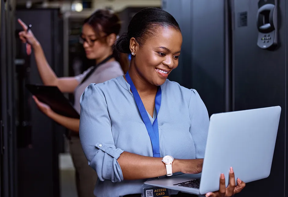 Smiling woman using a laptop in a server room