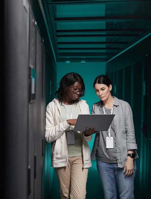 Two women using a laptop in a server room