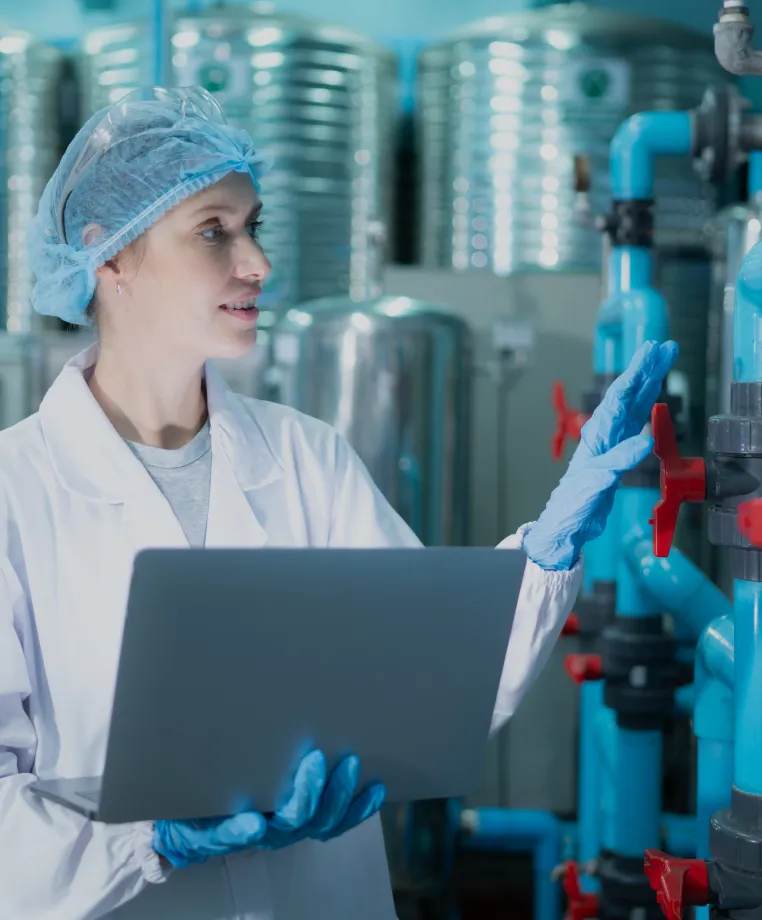 Lab worker using a laptop by industrial tanks