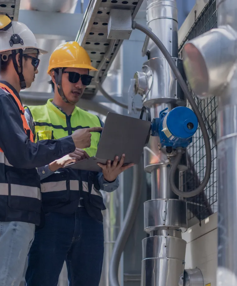 Two workers in hi-vis with a laptop at pipework