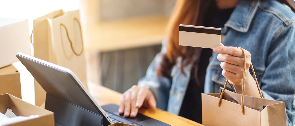 Person holding a card and shopping bag beside a laptop