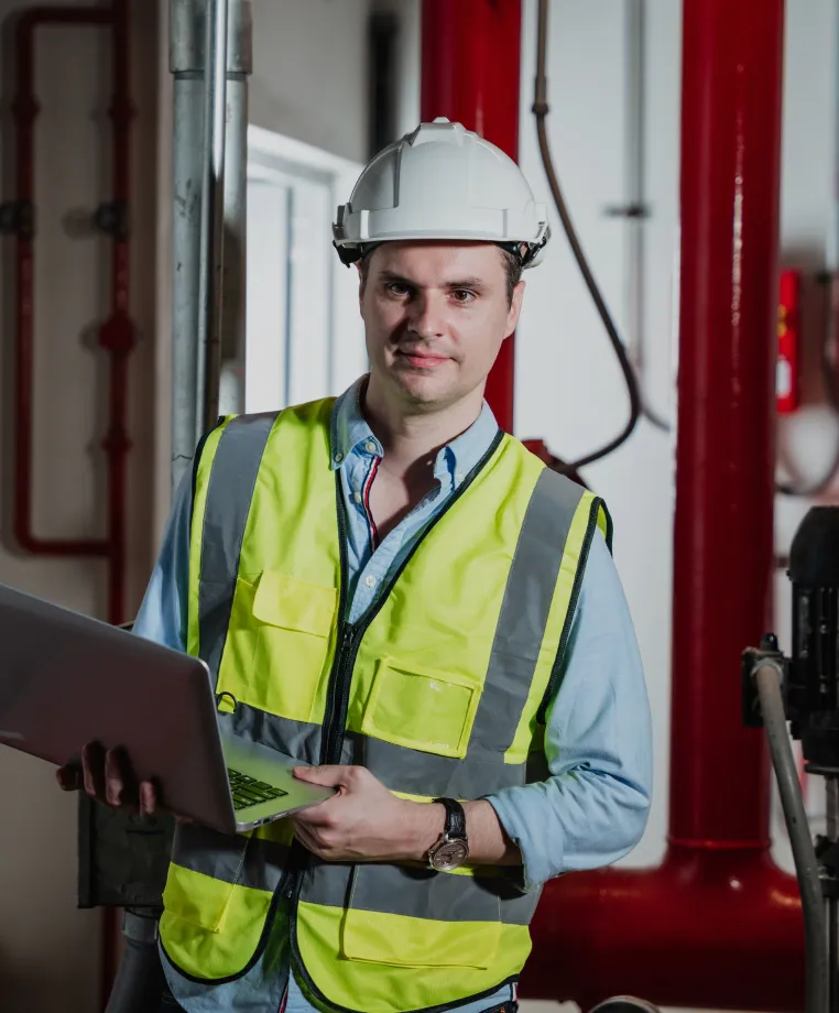 Worker in hi-vis holding a laptop in a plant room