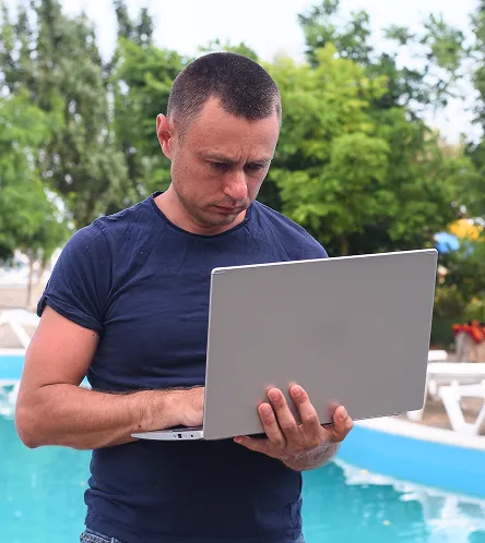 Man using a laptop by a swimming pool
