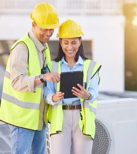 Two workers in hi-vis using a tablet by an air-conditioning unit