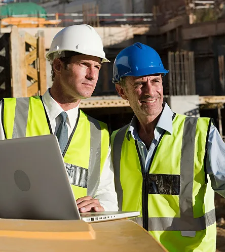Two construction workers in hi-vis using a laptop