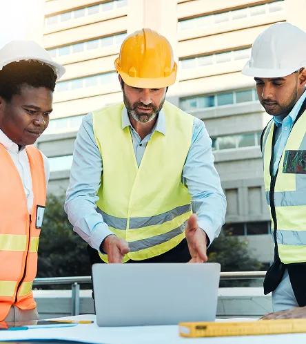 Construction workers in hi-vis reviewing plans on a laptop