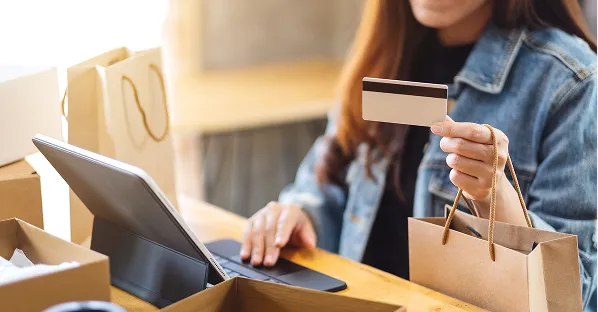 Person holding a card and shopping bag by a laptop