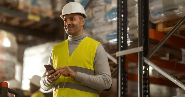 Smiling worker in hi-vis using a phone in a warehouse