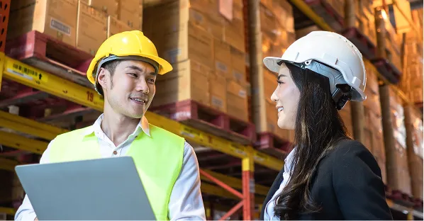 Two workers in hard hats using a laptop in a warehouse