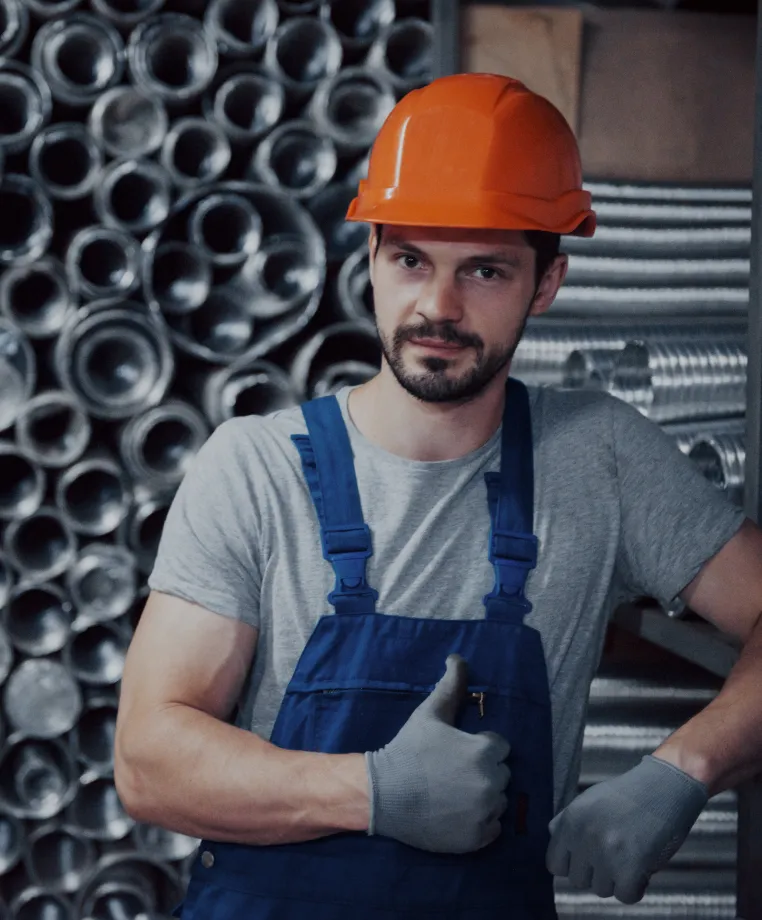 Worker in a hard hat with arms crossed by pipework