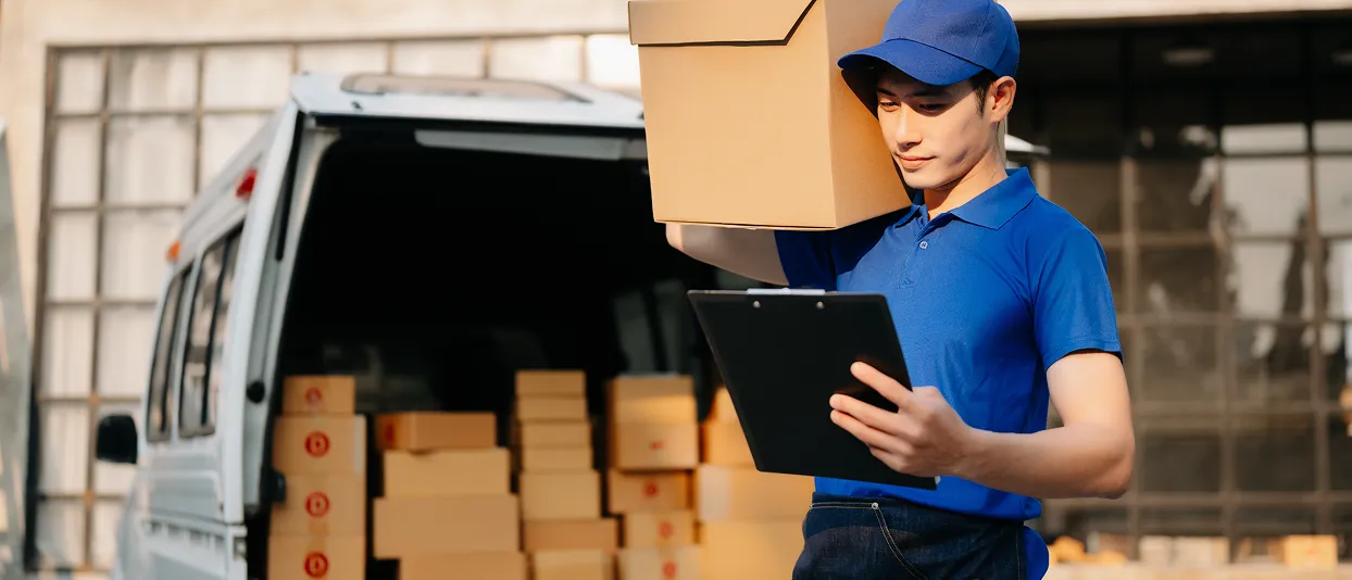 Delivery worker holding a box and clipboard at a van