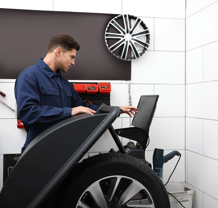 Technician using a laptop beside a vehicle in a service shop