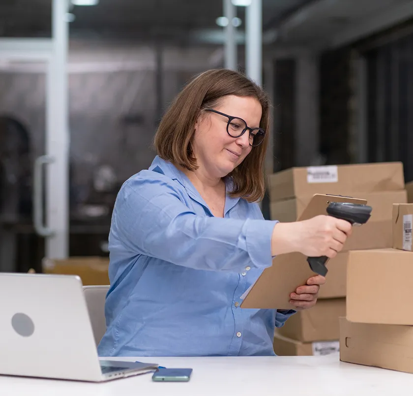 Woman scanning a parcel with a handheld scanner at a packing desk