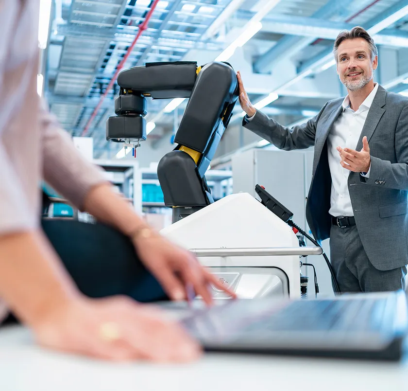Businessman beside a robotic arm in an automated facility