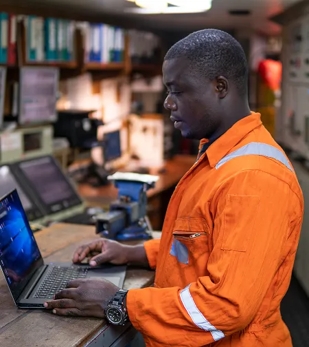 Worker in orange coveralls using a laptop