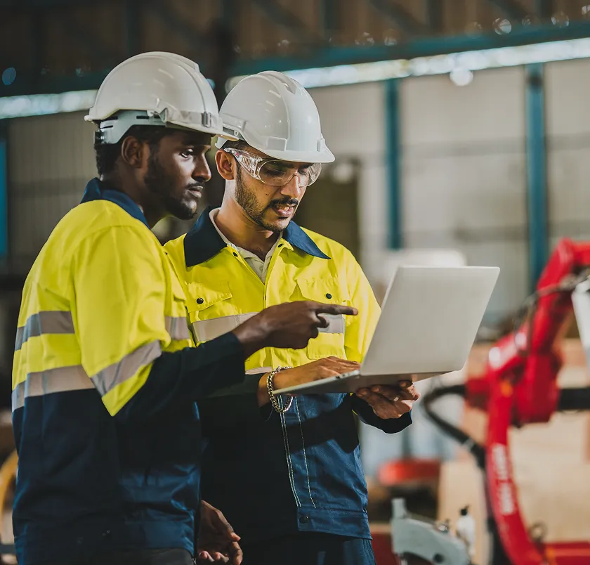 Two workers in hi-vis using a laptop beside machinery