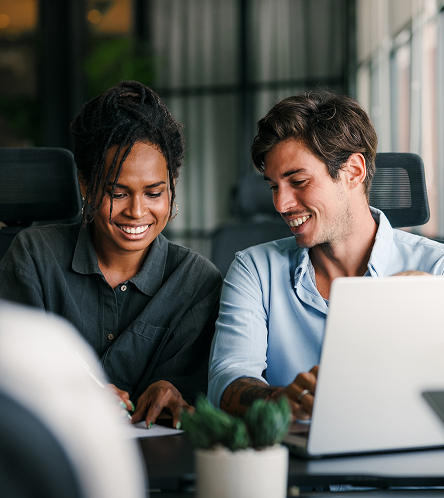 Two colleagues smiling at a laptop in an office