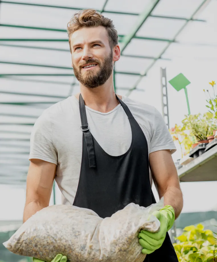 Smiling worker holding a bag of compost in a garden centre