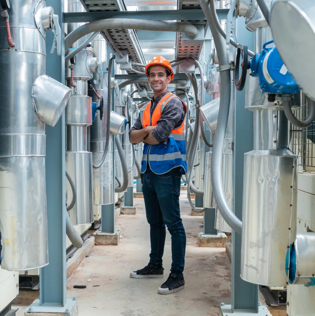 Smiling worker in hi-vis among industrial pipework