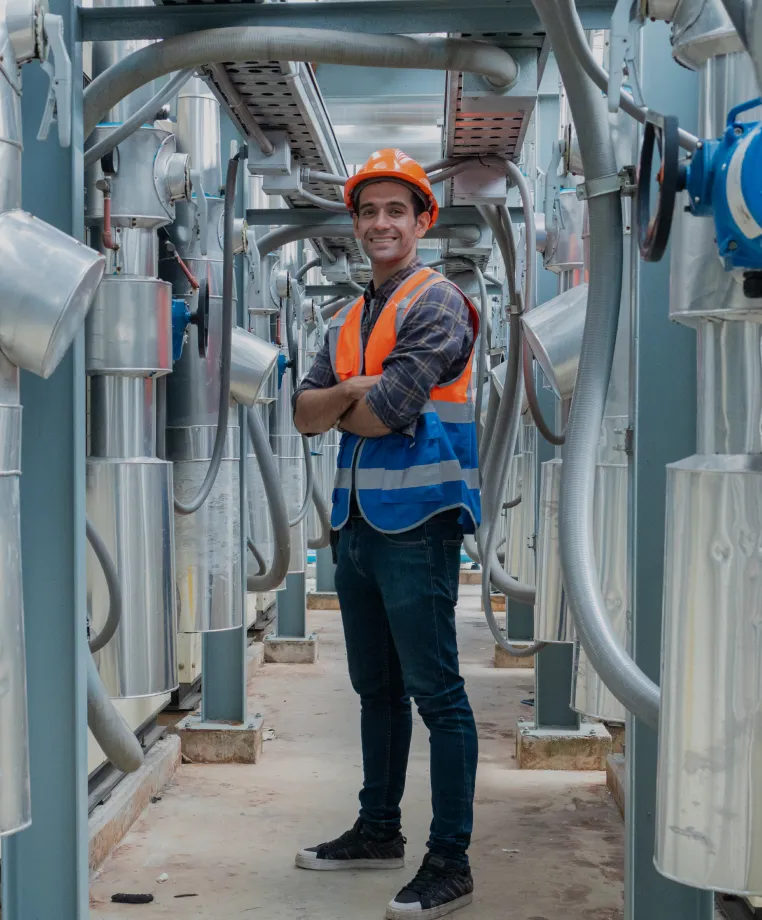 Smiling worker in hi-vis among industrial equipment