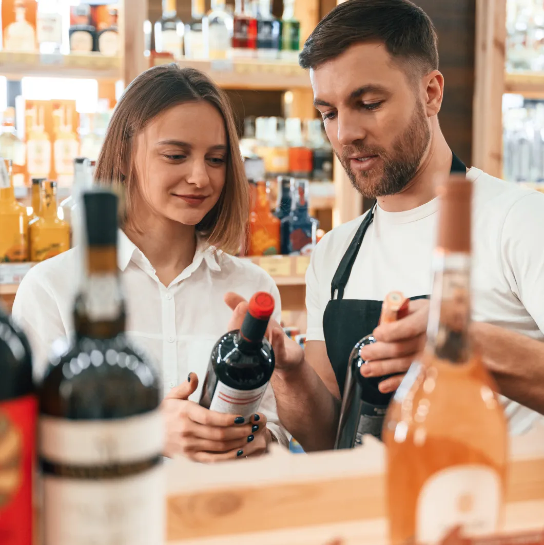 Two shop workers with wine bottles at a counter