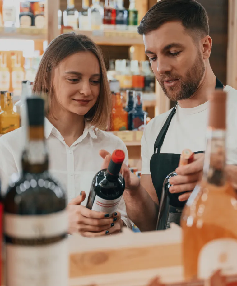 Two shop workers with wine bottles at a counter