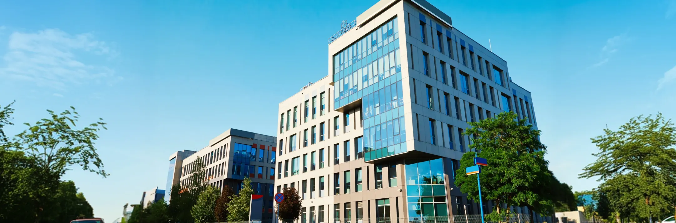 Modern office buildings with large glass windows under a clear blue sky with trees around.