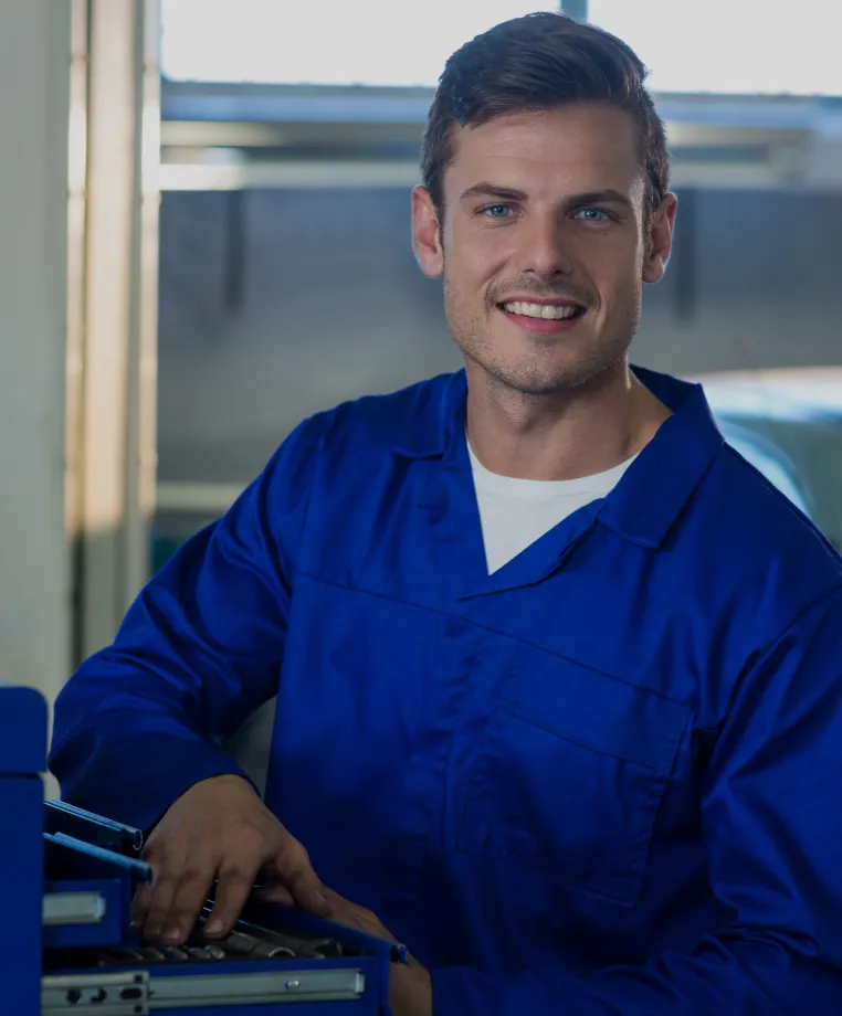 Smiling technician in blue overalls at a workbench