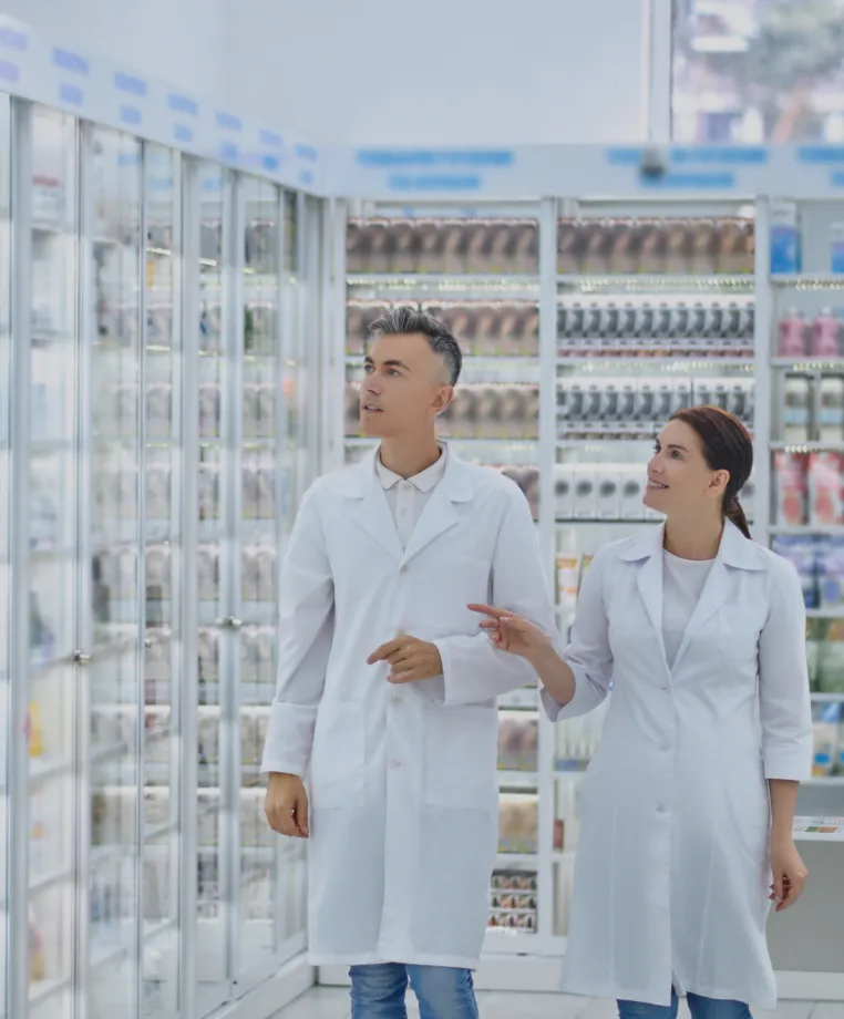 Two staff in lab coats inspecting a refrigerated retail aisle